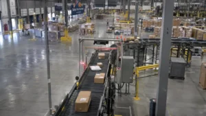 Industrial distribution hub showing an active conveyor lane and equipment charging docks in the foreground.