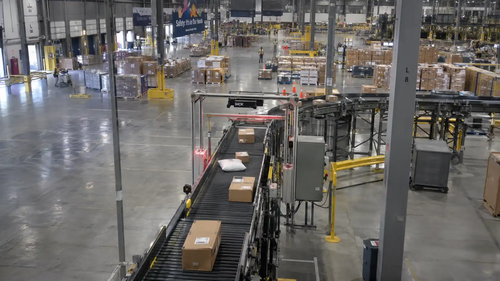 Industrial distribution hub showing an active conveyor lane and equipment charging docks in the foreground.