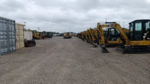 Outdoor industrial storage yard with heavy machinery and tagged containers awaiting transport.