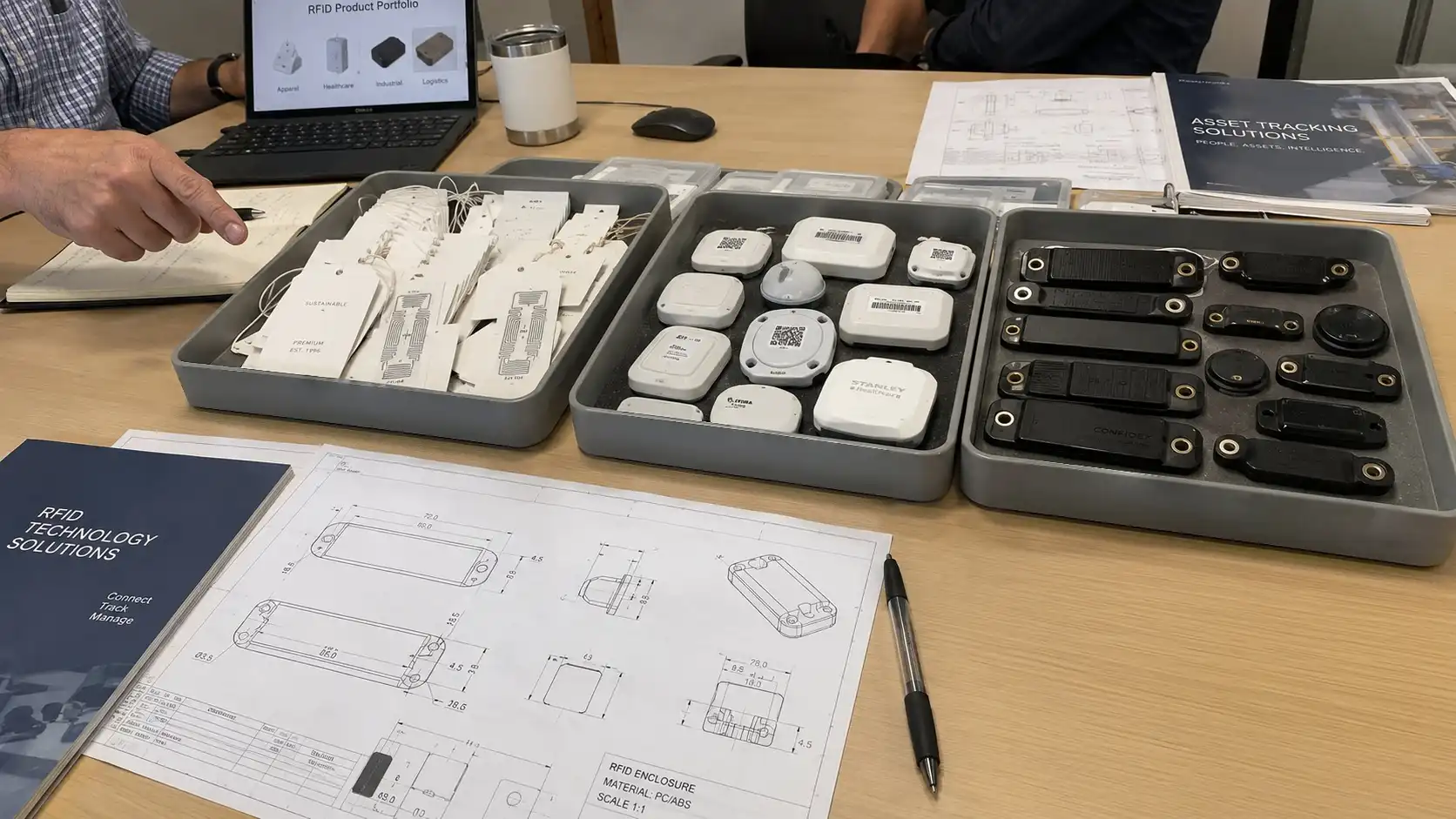 High-angle documentary overview of industrial parts, medical tracking badges, and retail tagged items arranged on an engineering desk.