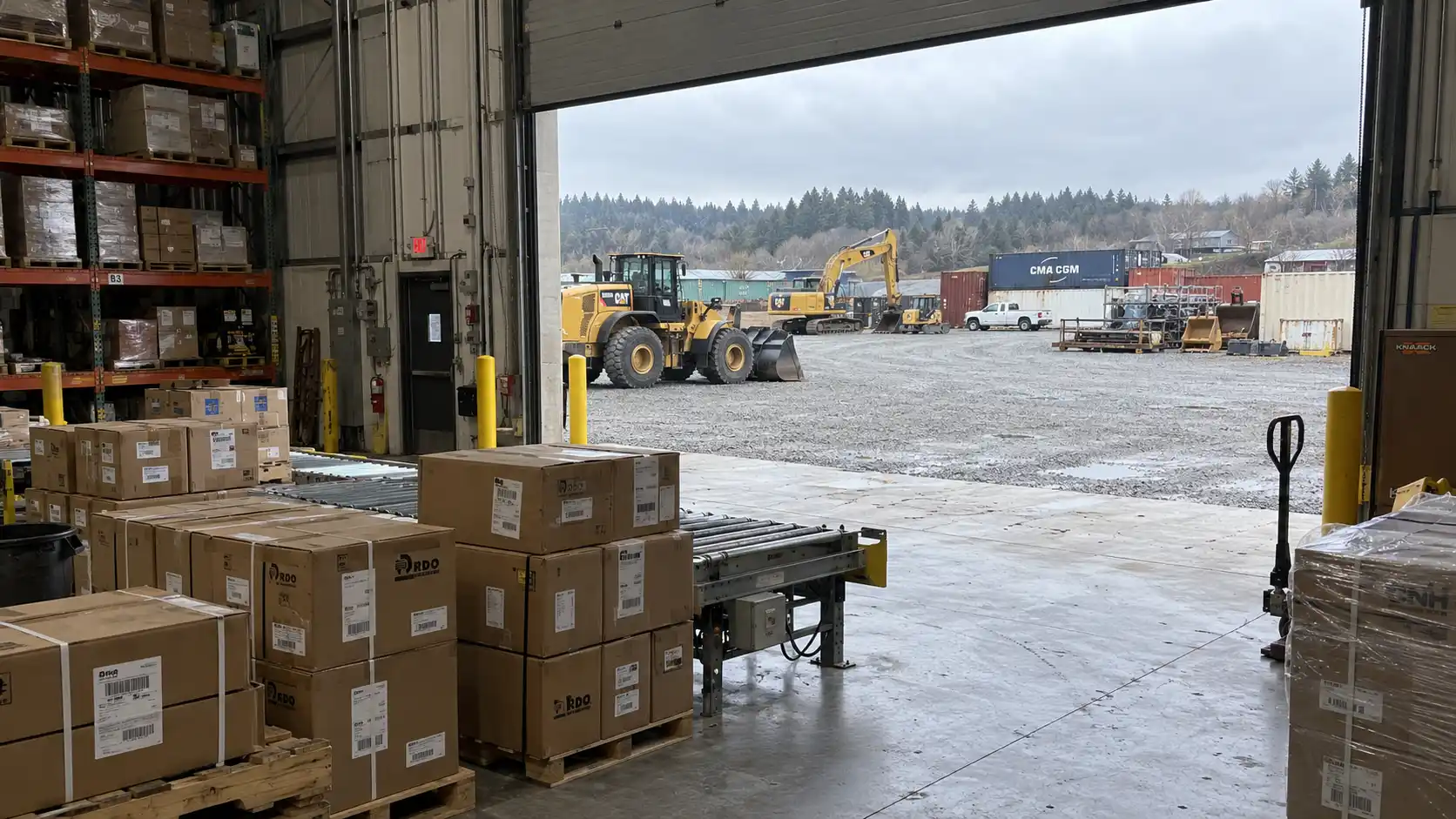 Industrial manufacturing facility showing an indoor conveyor checkpoint adjacent to an outdoor equipment staging yard.