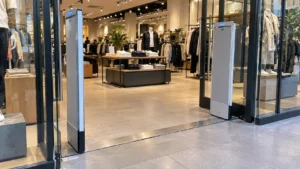 Storefront entrance of an apparel retailer featuring upright RFID loss-prevention pedestals near clothing displays.