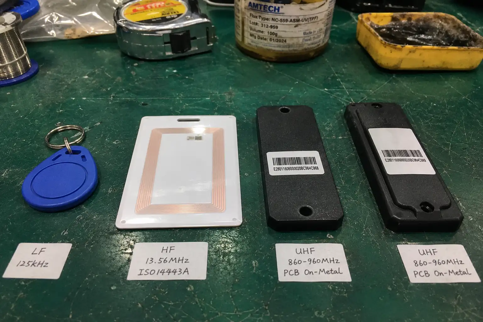 Hardware comparison of LF 125kHz keyfob, HF 13.56MHz card, and UHF 860-960MHz industrial tags on an ESD mat.