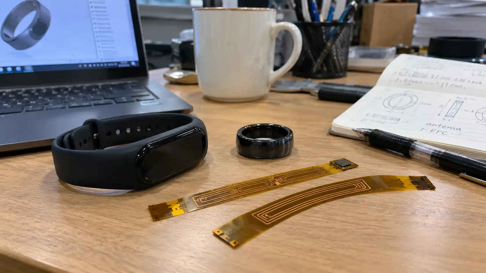 Hardware engineer's desk with wearable RFID prototypes including a silicone wristband and flexible antenna circuits.